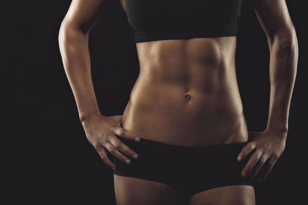 Close up of fit woman's torso with her hands on hips. Female with perfect abdomen muscles on black background