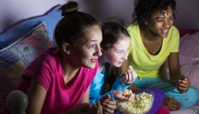 Preteen girls at sleepover watching tv, eating popcorn
