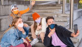 Young friends protected with face masks sitting outdoors with skateboards and bmx bicycle